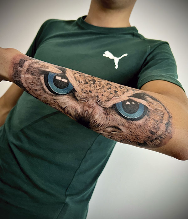 Tatuaje Buho real en el brazo en negro con ojos en color zul, en el brazo. De la Rocha Tattoo Cartagena, Murcia