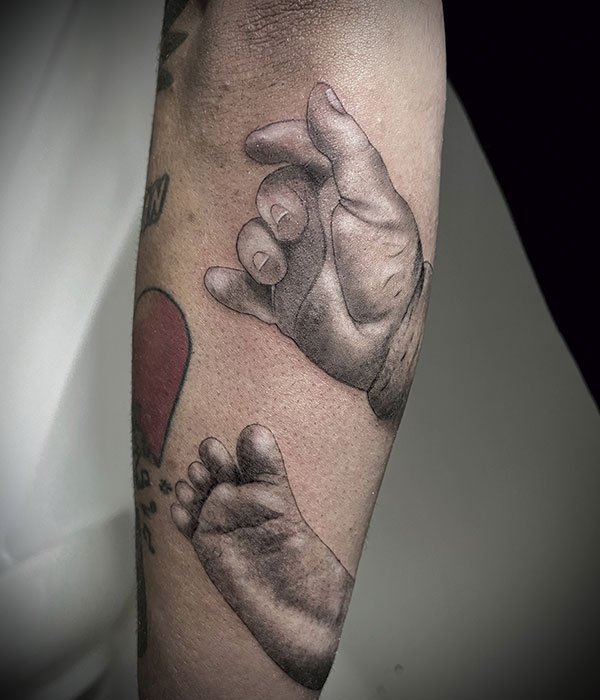 Tatuaje de mano y pie de recién nacido en el brazo, en negro, De la Rocha Tattoo Cartagena, Murcia